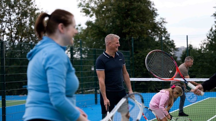 Sports Minister Stuart Andrew playing tennis alongside a family at refurbished tennis courts