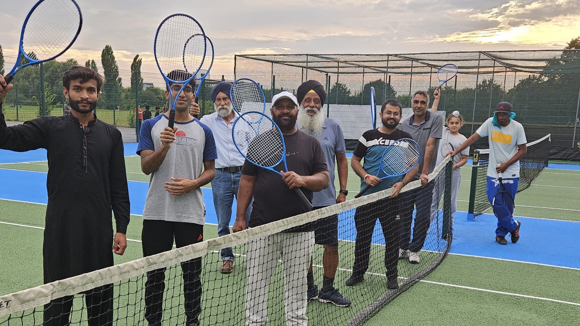 A group of men holding their tennis rackets up in the air while stood next to a tennis net on a park court