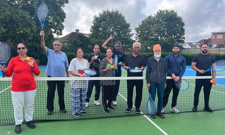 A group of men and women holding tennis rackets and tennis balls on a park tennis court