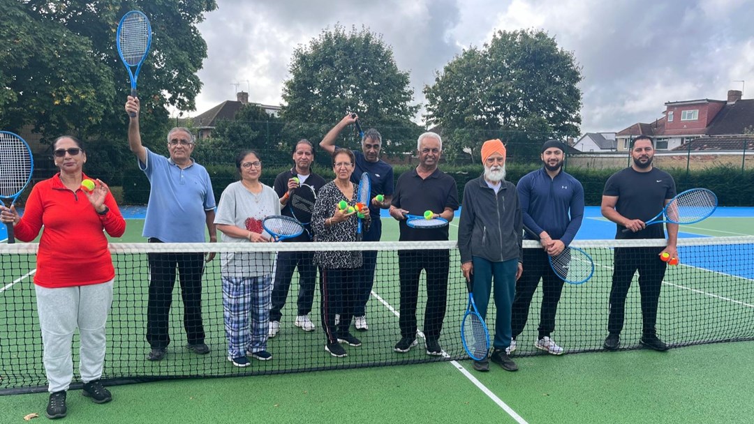 A group of men and women holding tennis rackets and tennis balls on a park tennis court