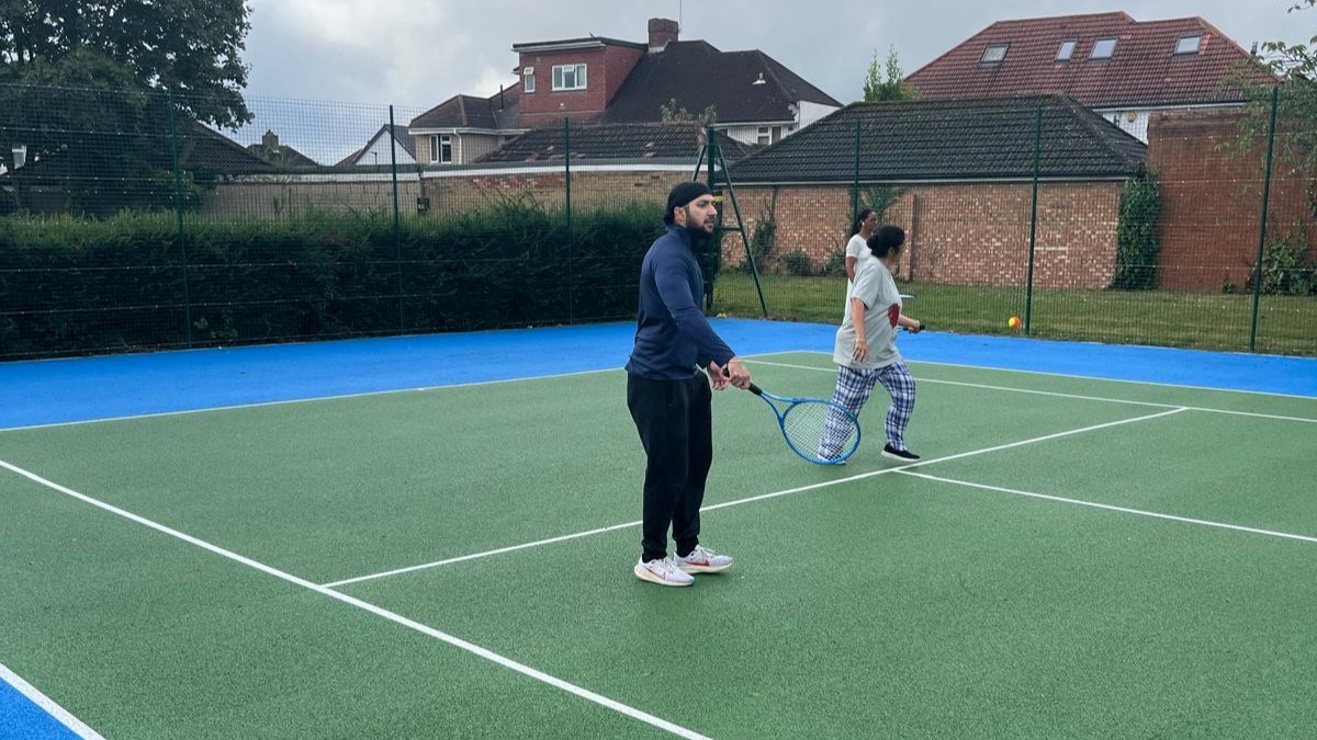 Three tennis players stood on a park tennis court playing tennis 