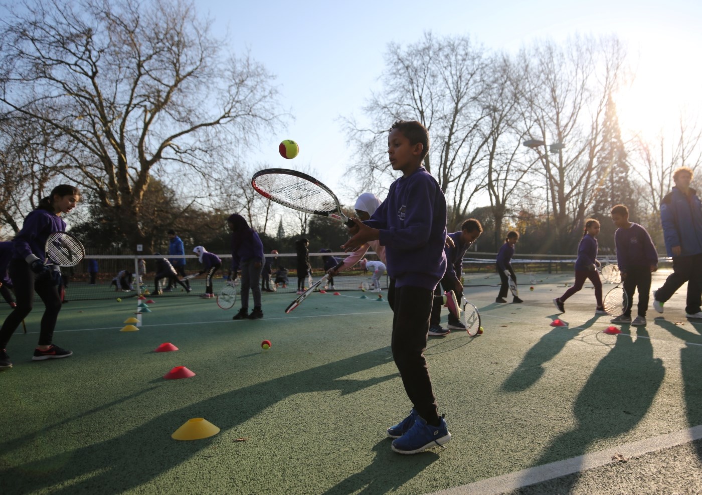 School children hitting tennis balls with rackets 