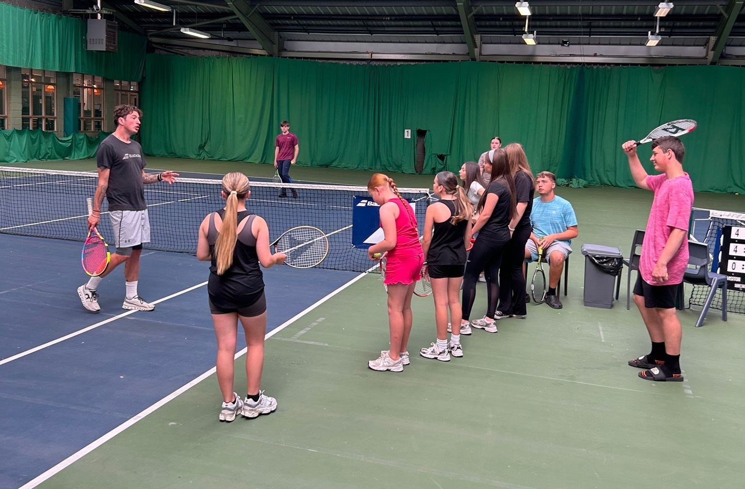 Children with tennis rackets playing tennis indoors with tennis coach