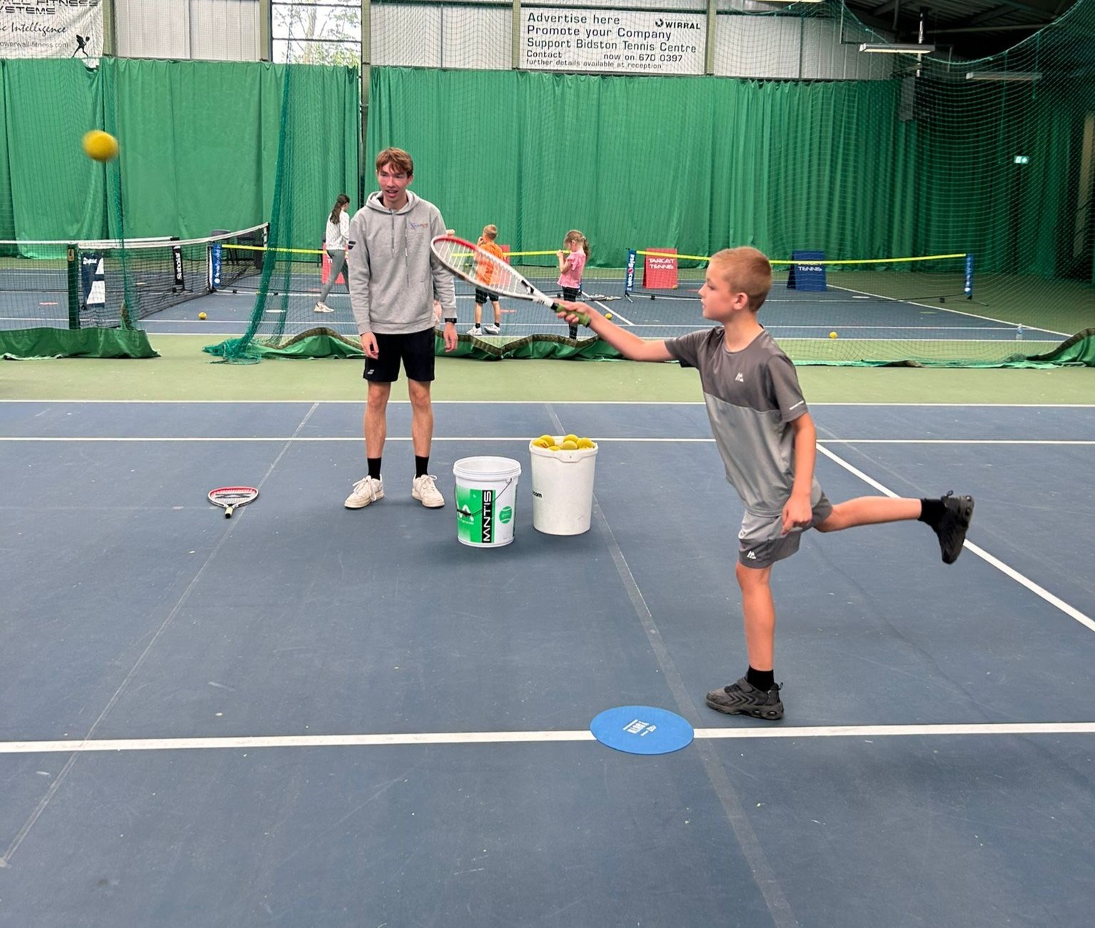 Child playing tennis indoors with coach 