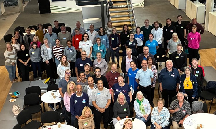A large group of people stand smiling looking up at the camera