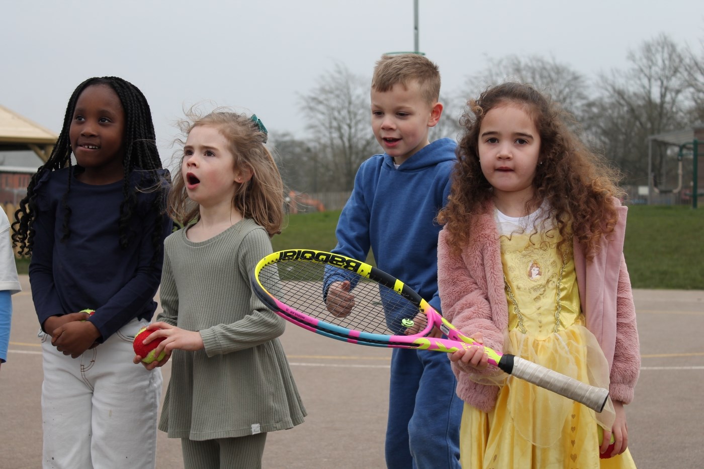 Four primary school students with tennis racket and ball standing in a line 