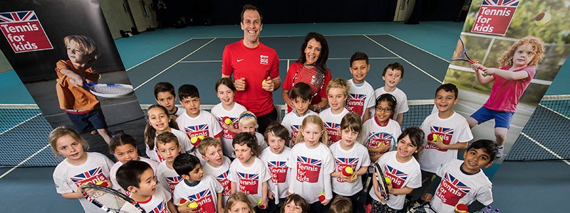 Group of children on a tennis court holding a tennis racket and ball