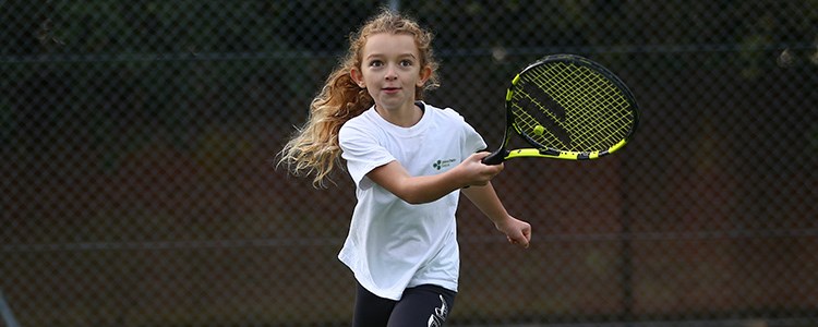 Young girl playing tennis with a black and yellow racket