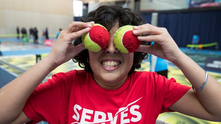 Boy holding tennis balls over his face smiling