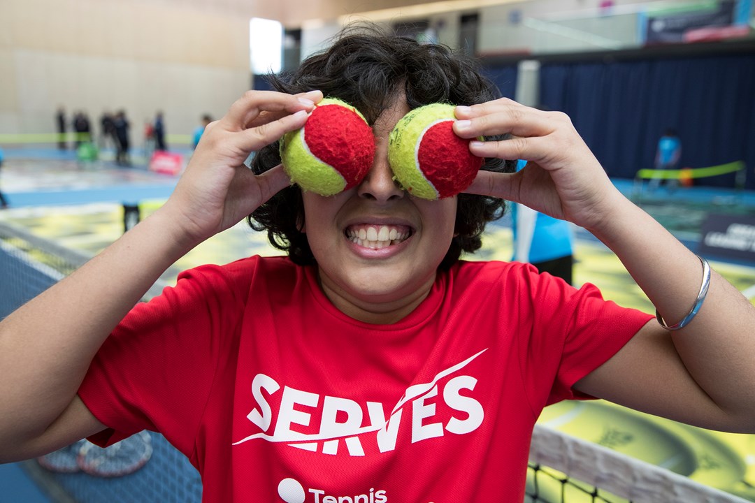 Boy holding tennis balls over his face smiling