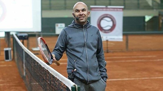 Leonardo Azevedo smiling on a tennis court holding a tennis racket