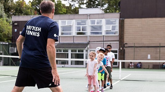 A coach coaching a group of young tennis students