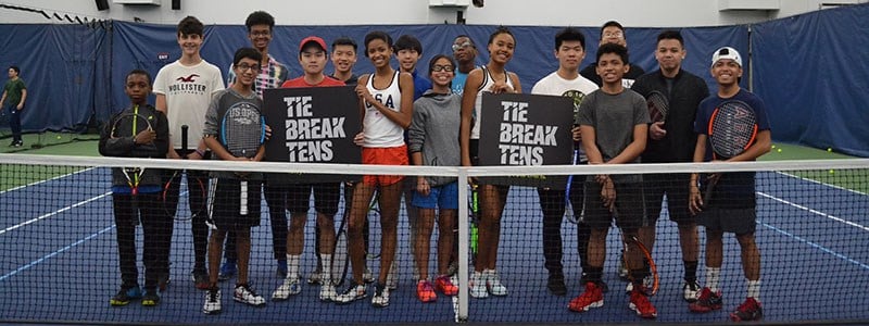 Group of junior tennis players on a court holding a 'tie break tens' sign