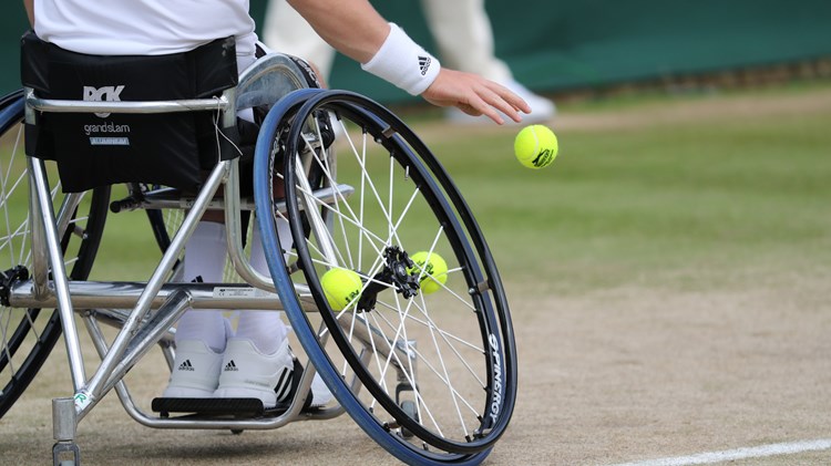 Close up of a wheelchair player bouncing the ball before serving on a grass court