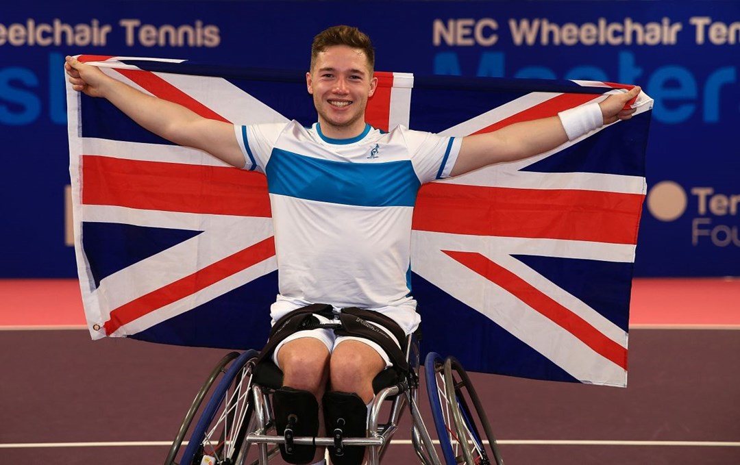 Alfie Hewett smiling holding up a Union Jack flag behind him