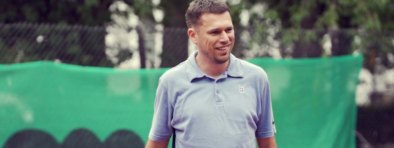 Steve mccann standing on a tennis court wearing a blue shirt and smiling 