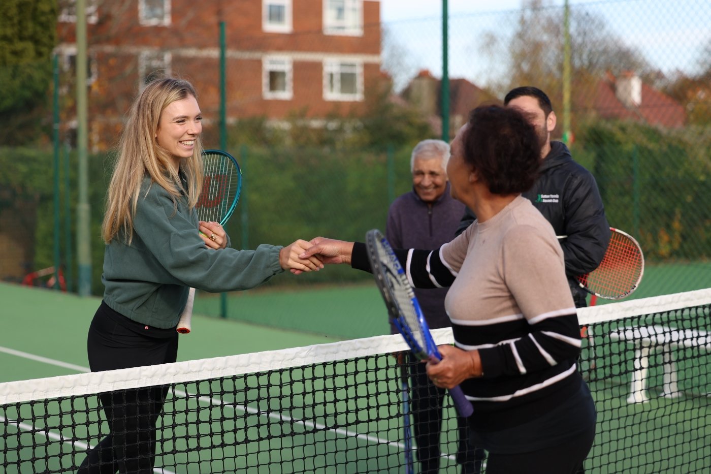 Two women holding tennis rackets shake hands over a tennis net