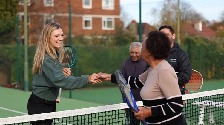 Two women holding tennis rackets shake hands over a tennis net