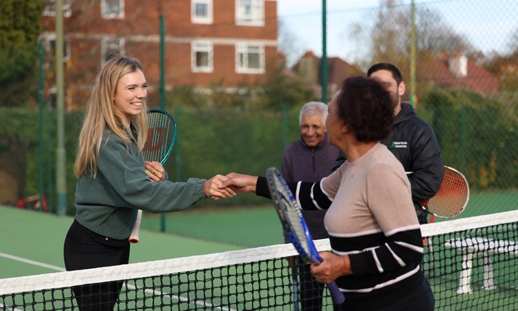 Two women holding tennis rackets shake hands over a tennis net