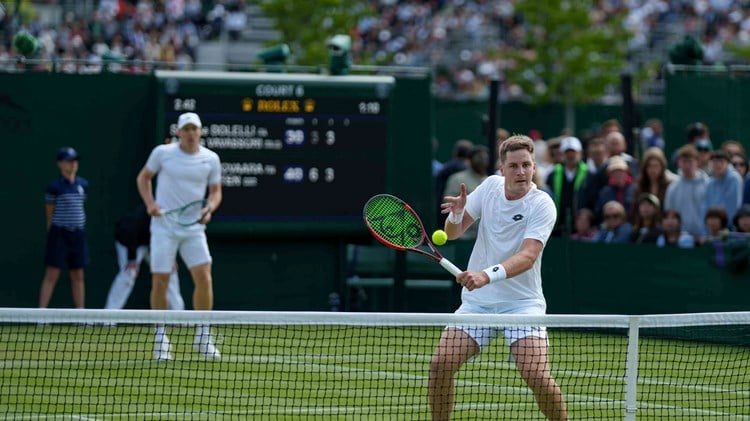 Henry Patten volleying at the net while Harri Heliovaara stands behind him on the grass court