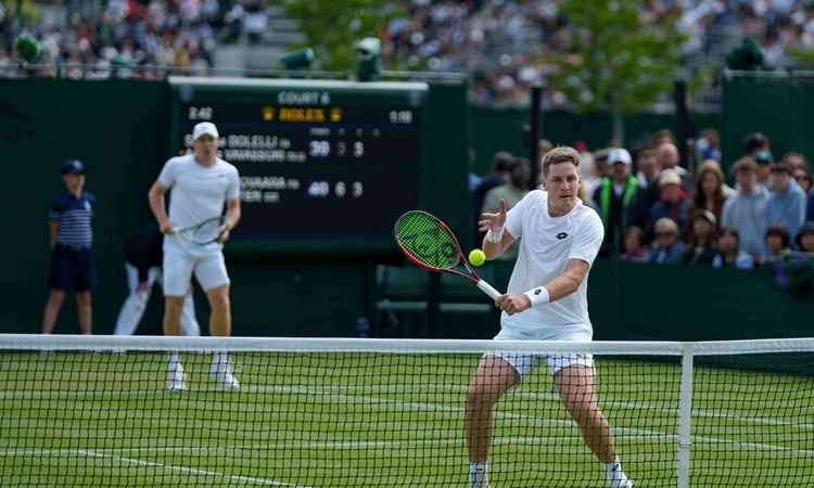 Henry Patten volleying at the net while Harri Heliovaara stands behind him on the grass court