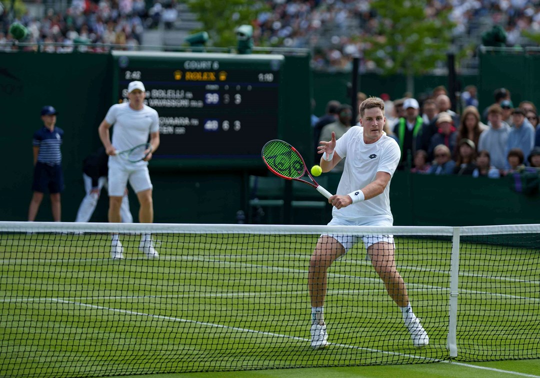 Henry Patten volleying at the net while Harri Heliovaara stands behind him on the grass court