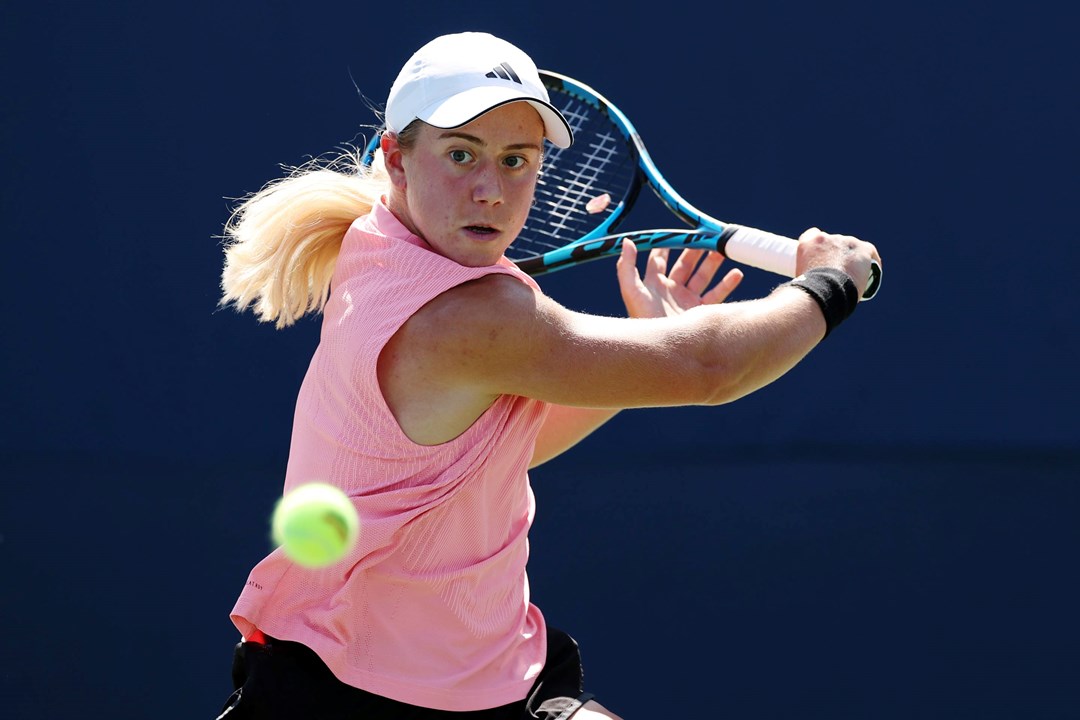 British tennis player Sonay Kartal wearing a pink top with a white Adidas hat while hitting a backhand slice at the US Open