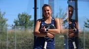 British padel player Catherine Rose leaning against the glass wall of a padel court wile holding her padel racket in her hands and wearing a blue 'LTA Padel'  kit