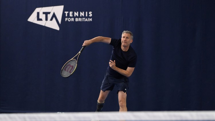 Comedian and tv presenter Adam Hills serving on court while playing para standing tennis at the National Tennis Centre in Roehampton