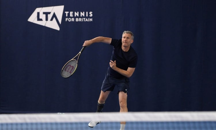 Comedian and tv presenter Adam Hills serving on court while playing para standing tennis at the National Tennis Centre in Roehampton