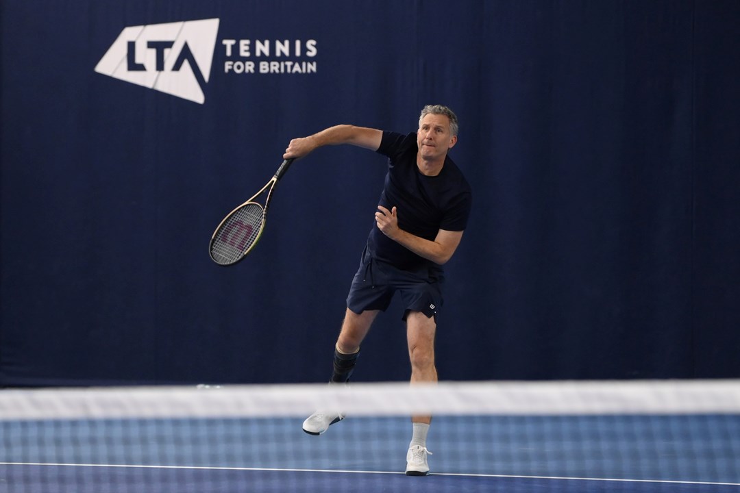 Comedian and tv presenter Adam Hills serving on court while playing para standing tennis at the National Tennis Centre in Roehampton