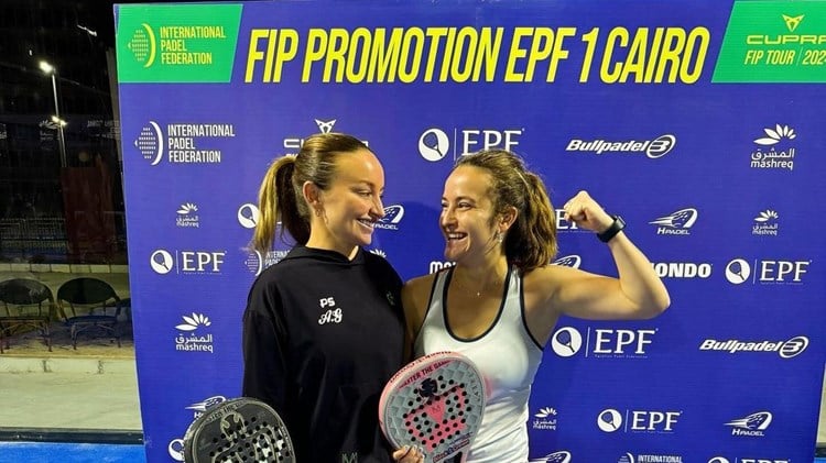 British padel player Aimee Gibson smiling while holding her padel racket in front of a 'FIP Promotion EPF 1 Cairo' sponsorship board