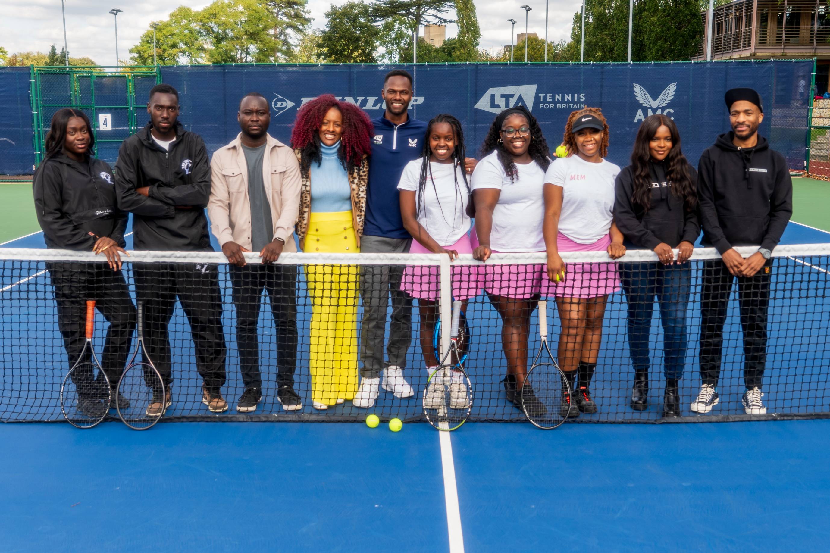 A group of people stood on a tennis court while holding the tennis net to form the Black Tennis Collective