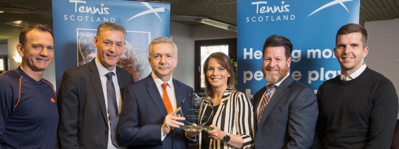 a group of winners lined up with two holding a glass tennis scotland trophy