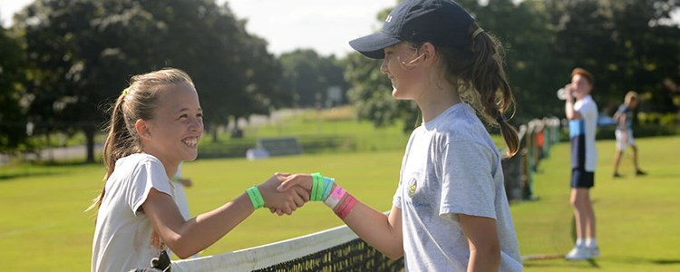 two young female tennis players shaking hands over the net
