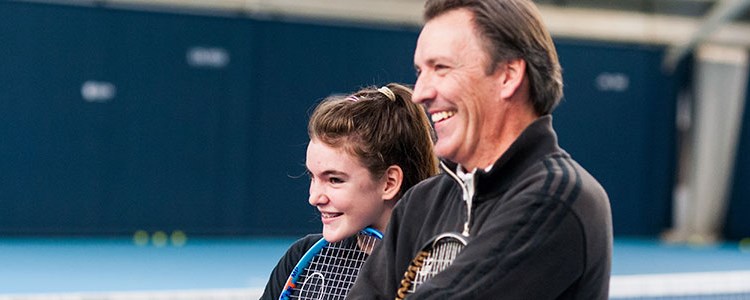 child and adult standing next to each other holding their rackets and smiling 