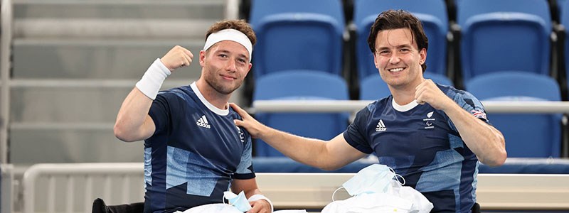 Alfie Hewett and Gordon Reid smiling together in their tennis gear pitchside next to the seats