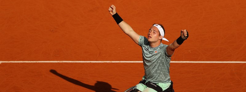 Alfie Hewett rejoicing with his arms raised on a clay tennis court