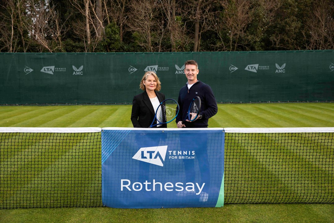 A male and female holding rackets and standing behind a tennis net