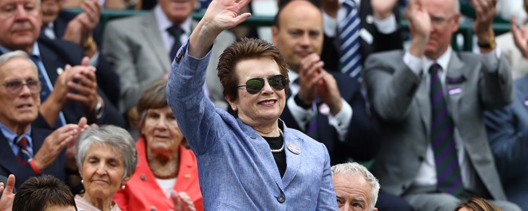 Billie Jean King standing up in a crowd waving and smiling