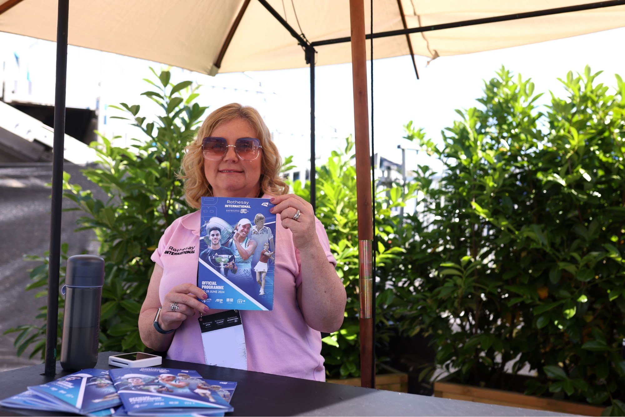 A volunteer wearing sunglasses, selling programmes at Eastbourne in the shade