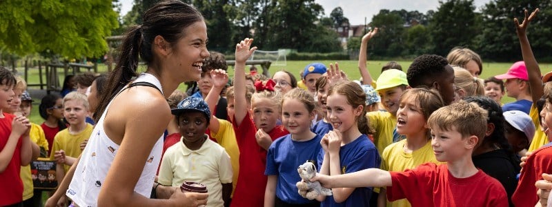 Emma Raducanu smiling with lots of children