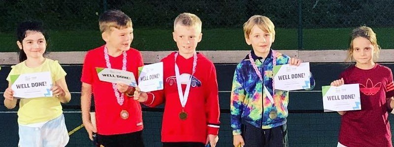 Five children lined up together holding a well done certificate on a tennis court