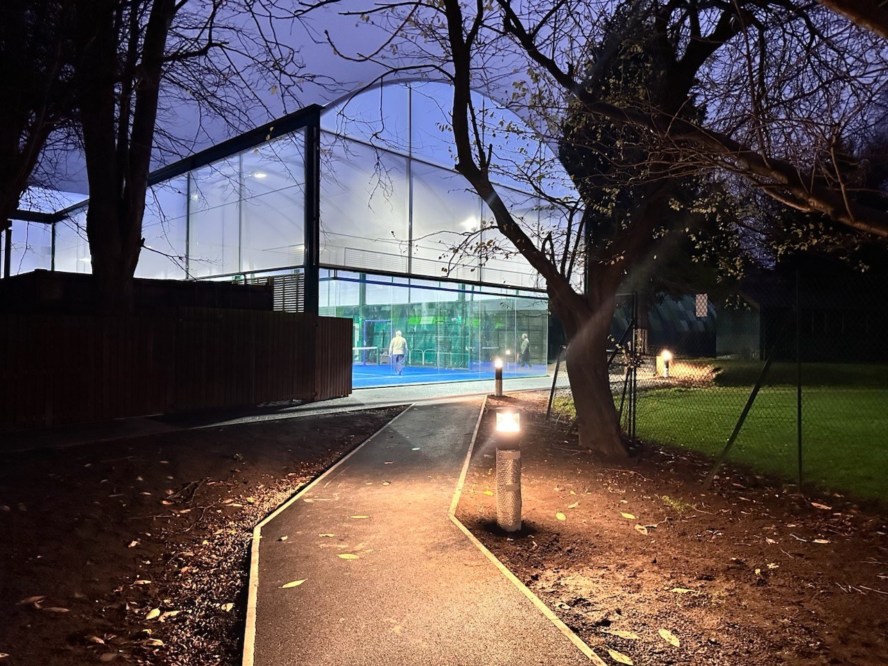 Padel court at twilight. A man can be seen in the distance playing padel.